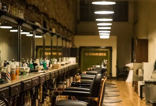 A long row of barber chairs under hanging lamps